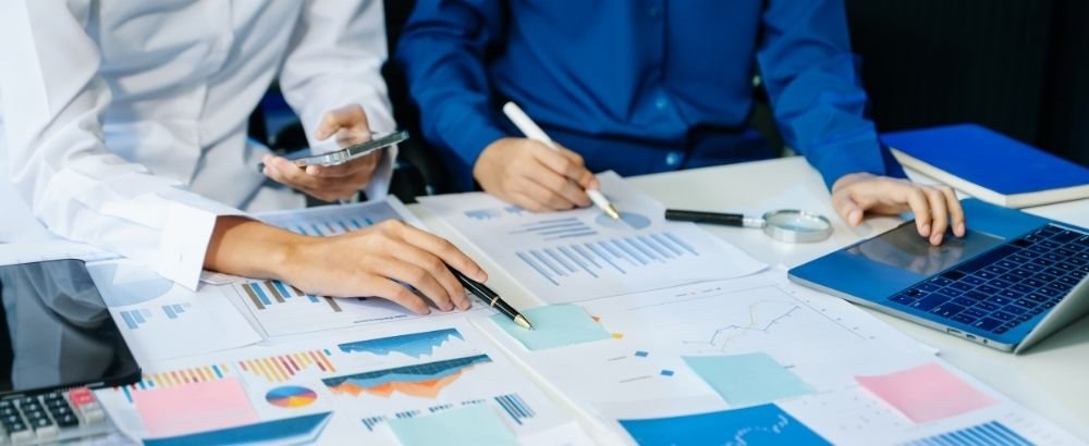 two employees holding pen on a hand and working looking at the laptop, papers kept on the table