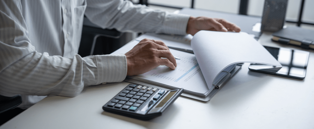 a man working on his office desk with pen paper and calculator